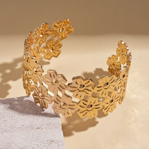 Detail of a wide gold-plated metal open cuff bracelet featuring intricate daisy cutouts