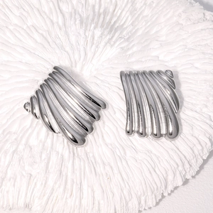 Macro shot of silver square stud earrings with vertical ribbed texture on coral surface