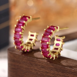 Macro shot of 925 silver earrings with square ruby-red zircon stones on a gold base