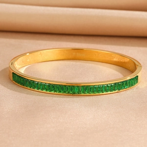 Gold stainless steel bangle with emerald-cut green zircons on champagne silk background