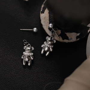 Macro shot of silver titanium steel bear earrings with mini pearls on dark textured surface
