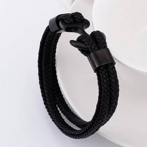 Close-up of black braided leather bracelet with matte metal anchor clasp on white ceramic