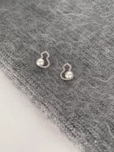Close-up of pearl and zircon hollow gourd stud earrings on grey knit fabric texture