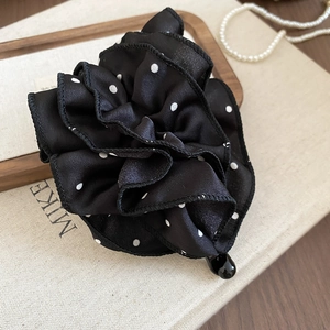 Détail d'une pince à cheveux fleur en tissu plissé à pois noirs sur plateau bois