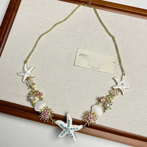Macro shot of gold necklace with white starfish, seashells and pink crystal floral accents