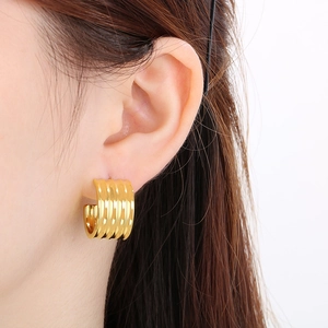 Détail de boucles d'oreilles créoles en forme de C dorées 18K avec design ondulé porté