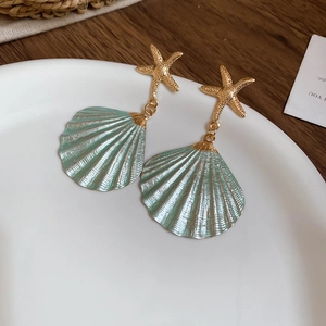 Detail of starfish studs and green seashell pendants on a minimalist white ceramic tray