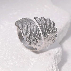 Silver feather wing open ring in stainless steel displayed on a textured white stone