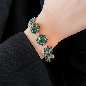 Close-up of vintage gold bracelet with emerald green floral stones on a wrist