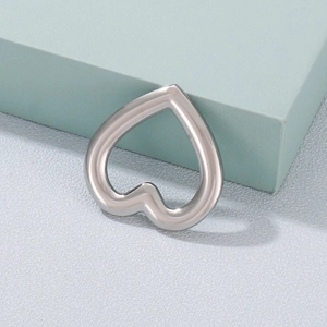 Minimalist silver heart-shaped hollow metal accessory placed on textured surface