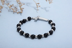 Vue détaillée du bracelet de perles noires avec pendentif croix sur un fond bleu texturé