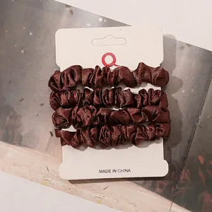 Detailed view of four brown satin scrunchies displayed on a white product card