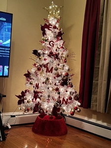 Detailed view of red sequin Christmas tree collar with festive ornaments on a white tree