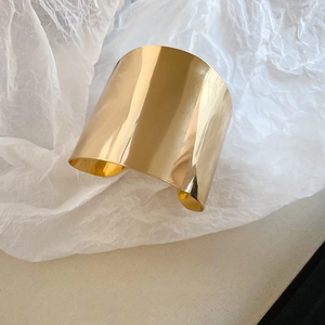 Detailed view of polished wide gold open cuff bracelet with glossy metallic finish