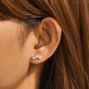Close-up of a gold crown stud earring with zircon tassels worn on a model ear