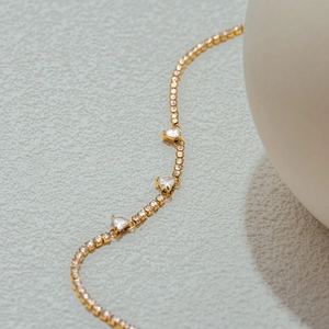 Macro view of gold-plated tennis bracelet featuring heart-shaped clear zircons