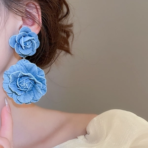 Detailed view of blue denim fabric double rose flower earrings worn on the ear