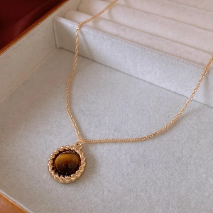 Macro shot of a vintage round tiger eye stone pendant on a gold twisted rope chain