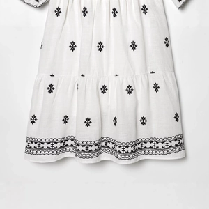 White dress with puff sleeves and black floral embroidery with layered pleated hem details