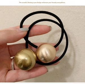 Close-up of golden metallic spherical bead on a black elastic hair tie held in hand