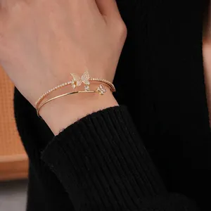 Double-layered gold cuff bracelet with zircon butterfly and flower charms on a wrist