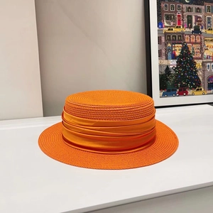 Detail of a bright orange flat-top straw hat featuring a pleated satin ribbon decoration