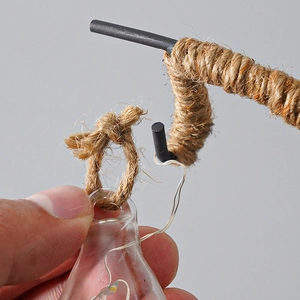 Detail showing hand hanging a hemp rope LED glass bulb onto a rustic black metal hook