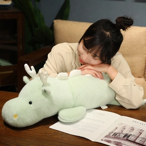 Close-up of soft light green plush dragon pillow with white horn and fin details