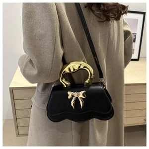 Detail of elegant black handbag featuring a wavy gold metal handle and 3D bow decoration