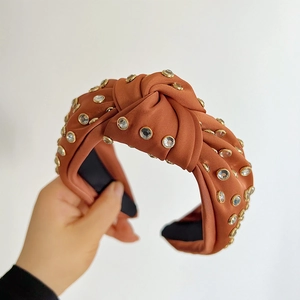 Macro detail of knotted caramel satin headband with sparkling crystal rhinestones and texture