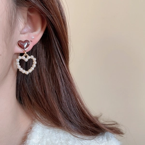 Close-up of double heart earrings with red enamel and white pearls on model