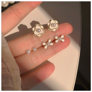 Hand holding elegant camellia, bow, and pearl stud earrings set in a gold finish