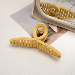 Detail of large matte ginger yellow hair claw clip on reflective surface with artistic cards