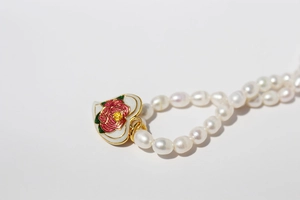 Macro shot of gold-plated heart pendant with red floral enamel on pearl necklace