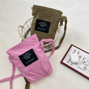 Detail of corduroy drawstring crossbody bags in olive green and pink with logo patch