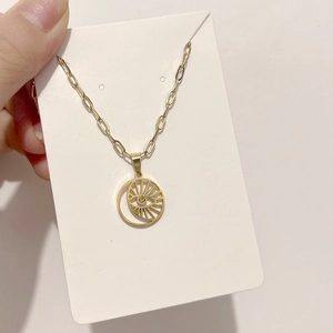 Detail of golden Evil Eye pendant with paperclip chain on a white card display
