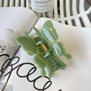 Detailed close-up of a large green butterfly hair claw clip resting on a magazine page