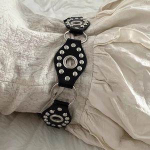 Detail of Y2K black leather belt with silver metal O-rings and punk rivet embellishments
