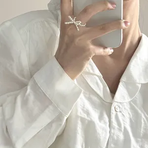 Detail of elegant woven pearl bow ring worn by a model against a white linen shirt
