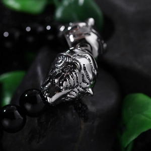 Macro view of black beaded bracelet featuring a detailed silver tiger head metal charm