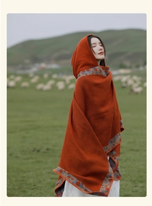 Detail of hooded knit poncho featuring intricate blue and orange patterned trim