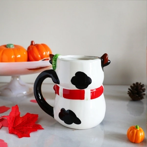 3D cow shaped ceramic coffee mug with black spots and red scarf in autumn setting