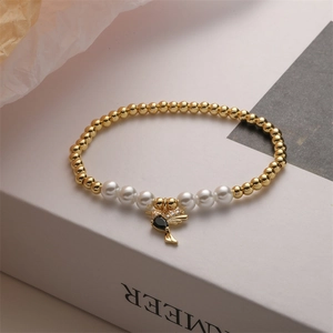 Detail of gold beaded bracelet with pearls and a black stone bird pendant on a book
