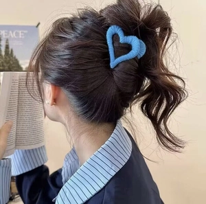 Blue heart-shaped plush hair claw clip shown on a high ponytail in a cozy setting