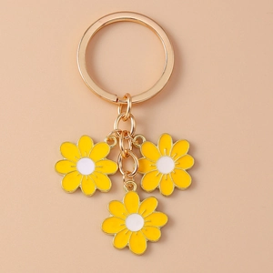 Detail view of golden keychain with three yellow daisy enamel floral charms on pink background