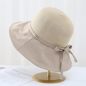 Beige straw sun hat with fabric brim and bow detail on a minimalist gold stand