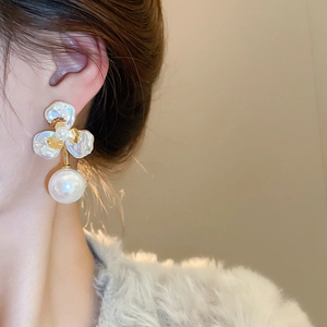 Close-up of gold-plated petal earrings with large round pearls worn by a model