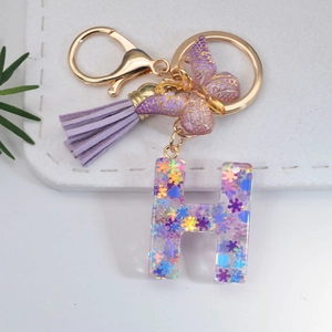 Macro detail of purple resin letter H keychain with star sequins and butterfly charm