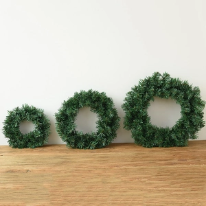Trois couronnes de Noël vertes de tailles variées sur un support en bois contre un mur blanc