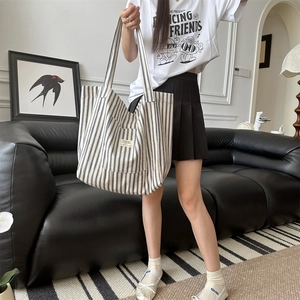 Close-up of a large blue striped canvas tote bag held by a model in a minimal room